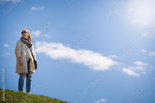 portrait of young blond woman standing on grass in the park and smiling. Happy girl walking and enjoying nature. Lifestyle