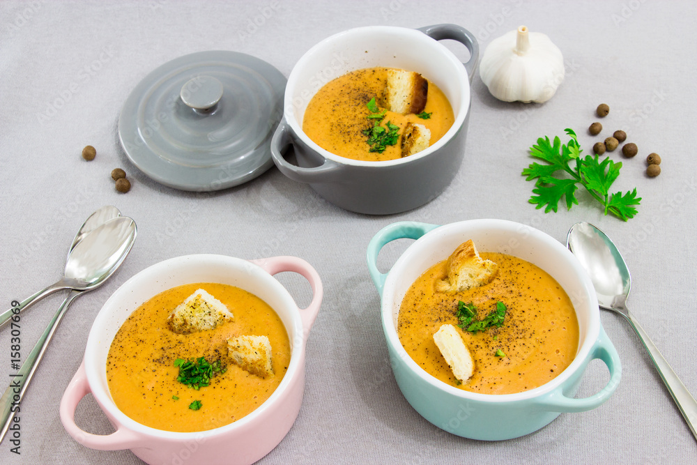 Three small serving pots or bowls with cream soup made of red lentils with rusks, spices and herbs parsley, coriander. On a light gray background. Three small serving pots or bowls with cream soup made of red lentils with rusks, spices and herbs parsley, coriander. On a light gray background.
