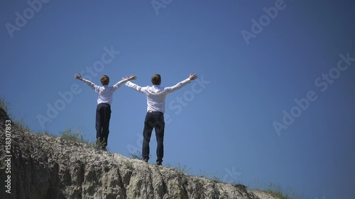 Father and son stand on the top of the hill and satisfied raised their hands to the sky celebrating the victory, free and happy, family celebration, winners, the chaste example for Father's Day