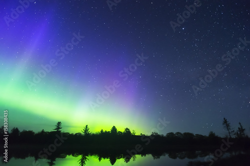 Northern lights vibrant in night sky full of stars and faint milky way