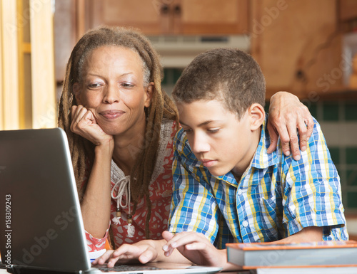 Quadro su tela Mother and teen son work in kitchen on laptop