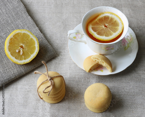 Artistic composition of tea with lemon in white porcelain cup and lemon cookies on grey linen cloth background