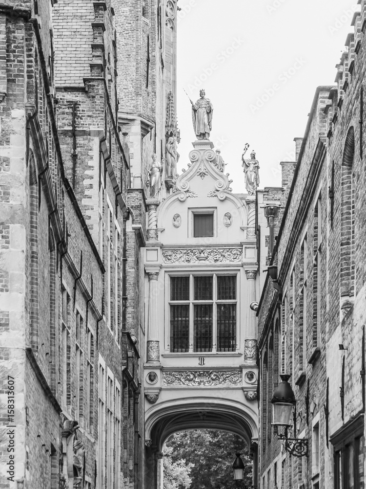 Bridge crossing between buildings over narrow Blinde-Ezelstraat, aka Blind donkey street, near Burg square, Bruges, Belgium. Black and white image.
