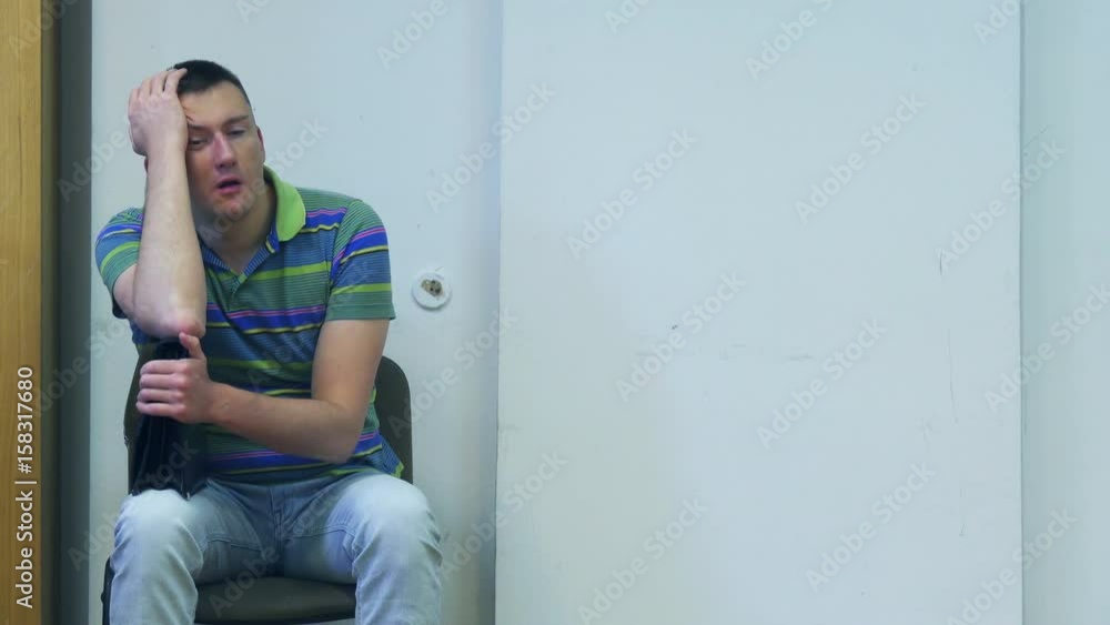 Exhausted waiting young businessman leans his head on his briefcase sitting in the waiting room Exhausted waiting young businessman leans his head on his briefcase sitting in the waiting room