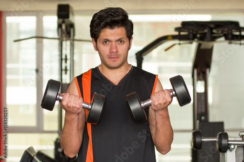 Handsome man doing biceps lifting with dumbbell on bench in a gym