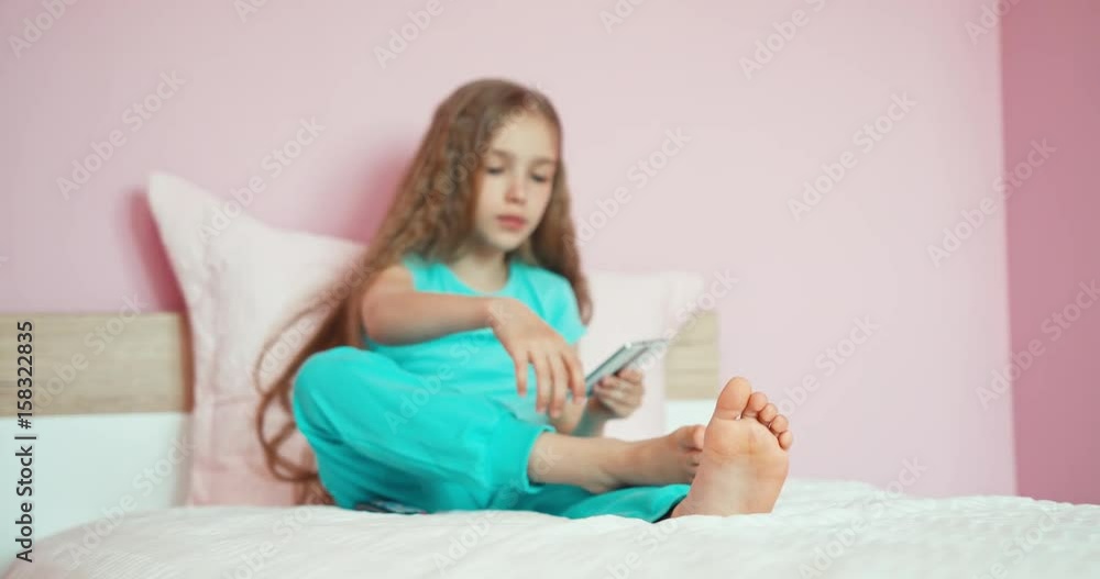 Child using smartphone in bedroom. Girl something typing and laughing Child using smartphone in bedroom. Girl something typing and laughing