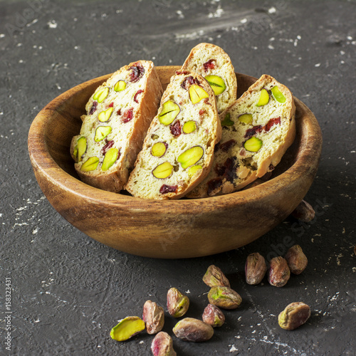 Traditional crispy Italian biscotti or cantuchini crackers with pistachios and dried cranberries in a bowl of olve wood on a dark background. Home classic healthy comfortable food photo