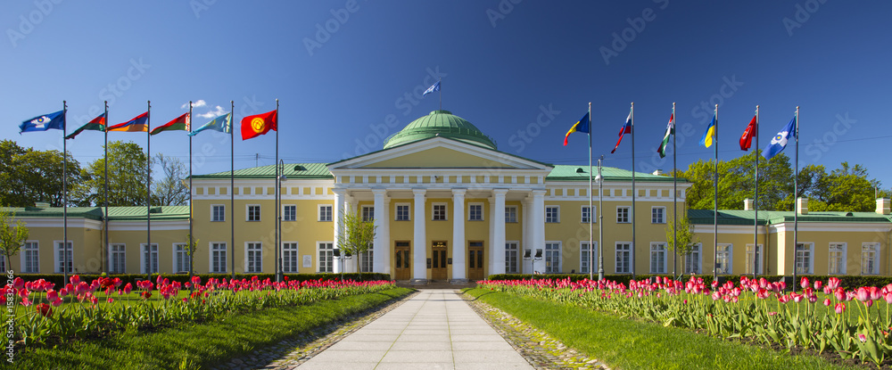  Tauride Palace, Saint Petersburg, Russia. Clear blue sky, green grass, red tulips and European flags in front of Palace.