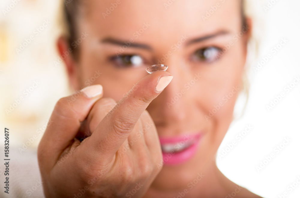 Young woman holding contact lens on finger in front of her face on white background., eyesight and eyecare concept