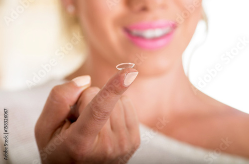 Young woman holding contact lens on finger in front of her face on white background., eyesight and eyecare concept