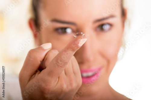 Young woman holding contact lens on finger in front of her face on white background.  eyesight and eyecare concept
