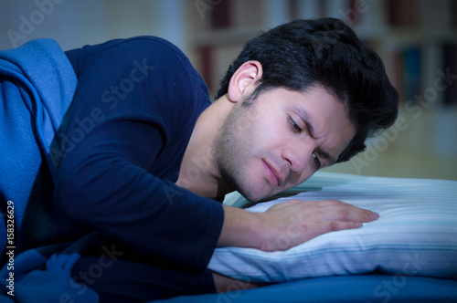 Handsome young man in bed with eyes opened suffering insomnia and sleep disorder fixing his pillow