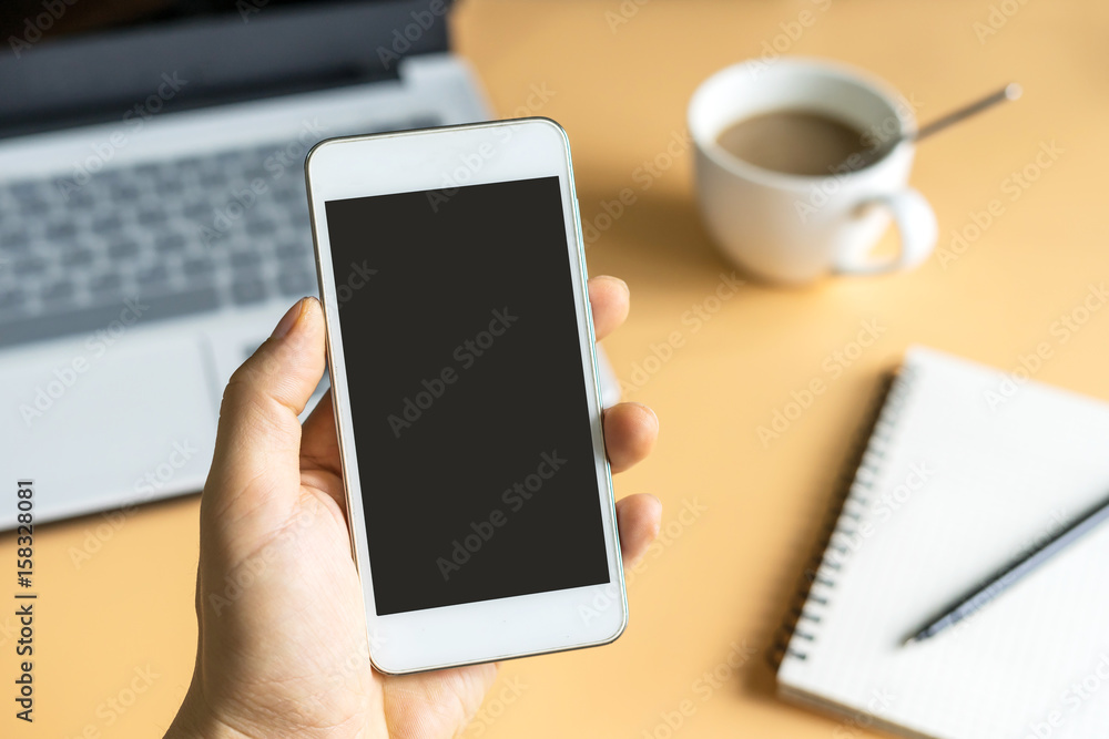 A man holding smart phone with laptop and coffee background A man holding smart phone with laptop and coffee background