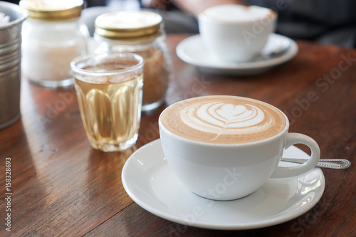 A cup of coffee with leaf pattern in a white cup on wooden background.