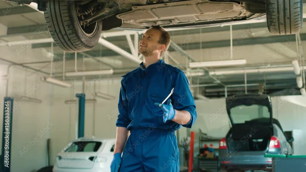 Caucasian auto mechanic man in blue uniform standing at autoservice and using wrench for screws. Indoor. Caucasian auto mechanic man in blue uniform standing at autoservice and using wrench for screws. Indoor.