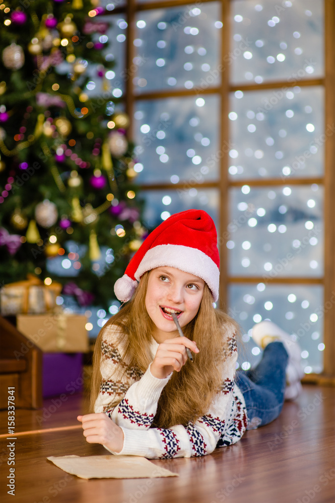 Thoughtful teen girl in red christmas hat writes letter to Santa Claus