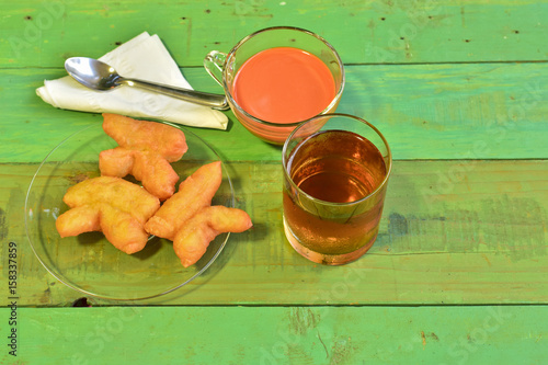 Hot tea and Youtiao (Cahkwe, Cakwe, Kueh, Kuay, Chinese Doughnut, traditional Chinese Snack, oil-fried pastry ,fried breadstick) put on old green wooden table. East and Southeast Asian cuisines photo