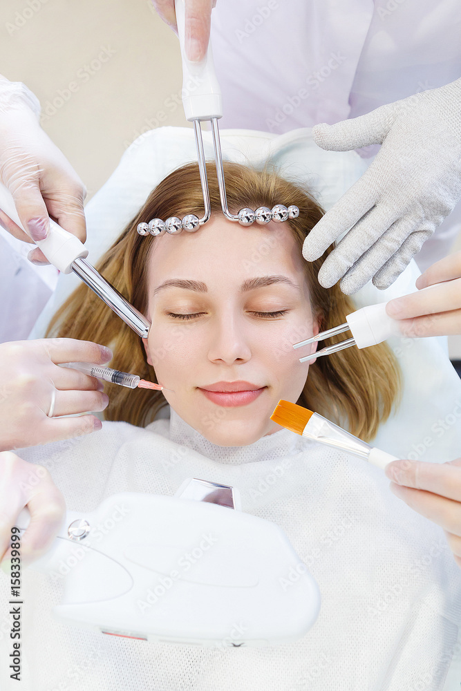 Naklejka premium Beauty treatment and cosmetology concept. Hands of several beauticians holding their respective equipment near patient face
