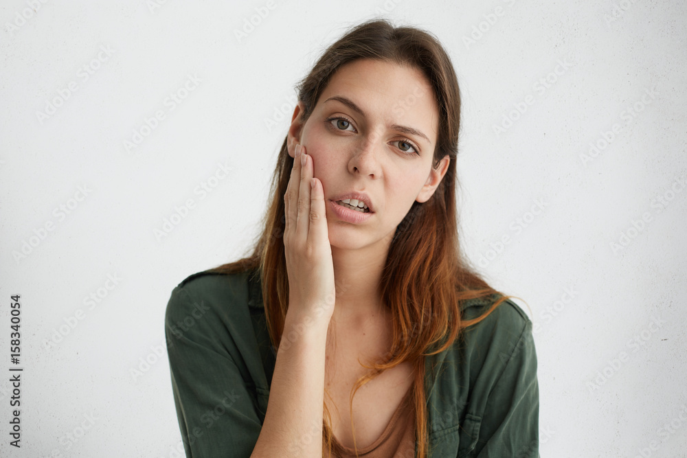 Horizontal portrait of pretty sad woman with bright dark eyes and straight hair holding hand on cheek looking upset after hard work. Exhausted female student after session having sad expression Horizontal portrait of pretty sad woman with bright dark eyes and straight hair holding hand on cheek looking upset after hard work. Exhausted female student after session having sad expression