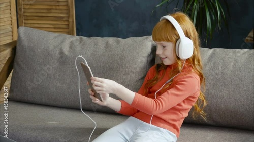 Little girl in headphones using smartphone, making a selfie 