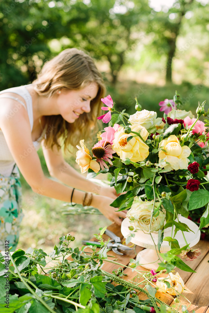 bouquet, people and floral arrangement concept - woman with beautiful bouquet of pink peonies, yellow and white roses, carnations and daisies, female florist at the table with flowers in garden bouquet, people and floral arrangement concept - woman with beautiful bouquet of pink peonies, yellow and white roses, carnations and daisies, female florist at the table with flowers in garden