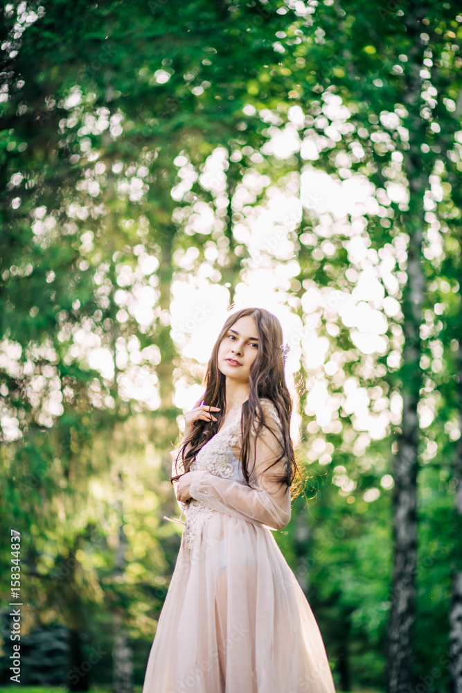 beautiful young girl bride brunette in delicate Bridal boudoir gown of lace and tulle in beige color is outdoors, in a Park with trees, birches, profile beautiful young girl bride brunette in delicate Bridal boudoir gown of lace and tulle in beige color is outdoors, in a Park with trees, birches, profile
