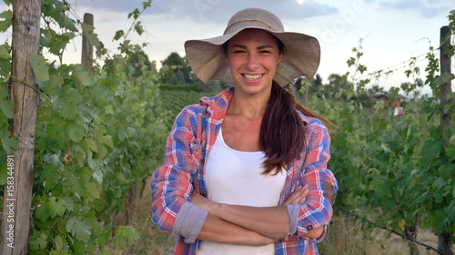 Beautiful smiling girl (woman) farmer watching over grape fields, in a straw hat and in a shirt, greens background. Concept ecology, wine, bio product, inspection, water, natural products, agriculture