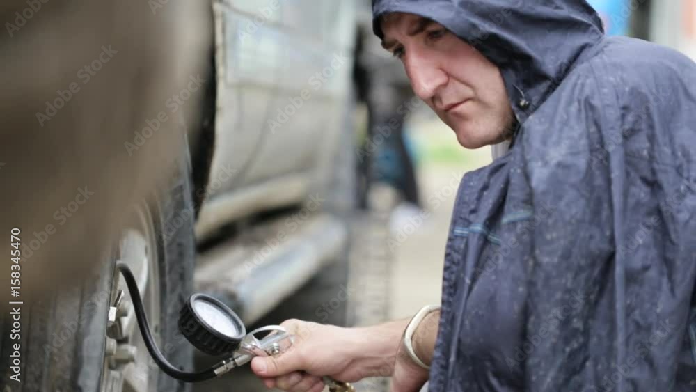 Man in raincoat pumping wheels of SUV at roadside Man in raincoat pumping wheels of SUV at roadside