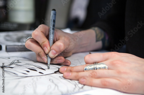 Girl tattoo artist draws a sketch. Close-up of hands photo