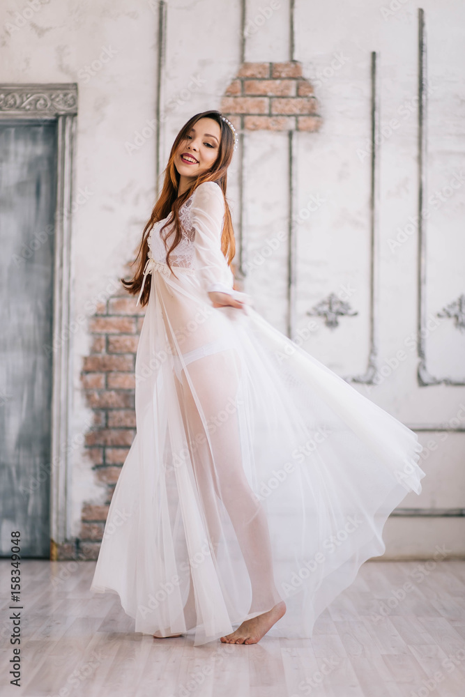 Morning of the bride. Beautiful young woman in elegant white robe walking. Dress developing in the wind. Happy lady in a wedding attire is spinning, boudoir photography