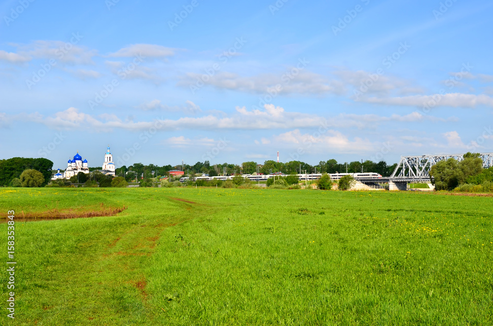 Bogolyubovo, spring landscape with a church, a green meadow and a high-speed train