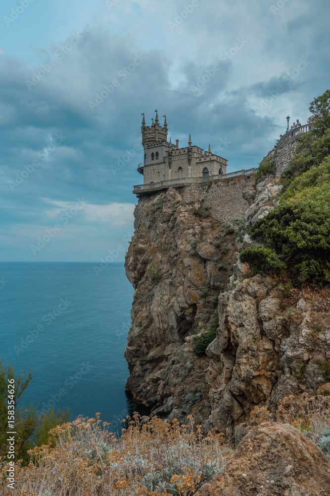 The Swallow's nest (Lastochkino gnezdo) castle, Gaspra (Yalta), Crimea, Russia. A castle on the rock over the Black sea, a cloudy sky at the background, a trees and bushes on the rock.