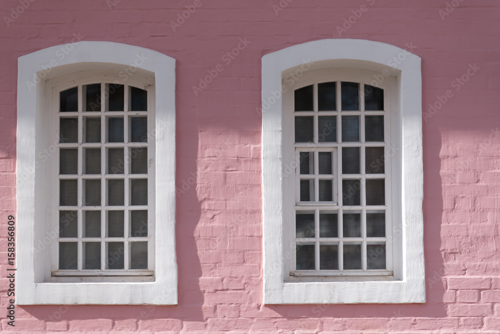 Part of facade of old building with pink cracked brick walls and semi-circular windows.