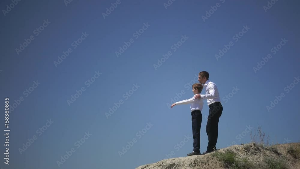Father and son stand on a hill and look confidently into the distance, dreaming of a happy future of the family talking about friendship and freedom Father and son stand on a hill and look confidently into the distance, dreaming of a happy future of the family talking about friendship and freedom