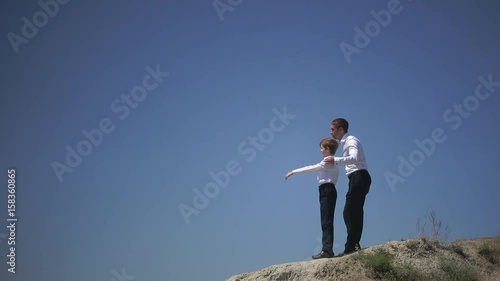 Father and son stand on a hill and look confidently into the distance, dreaming of a happy future of the family talking about friendship and freedom