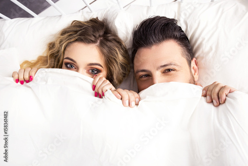 Young happy couple lying together in bed