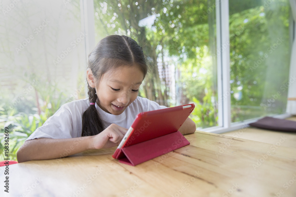 Little asian girl using computer tablet in living room with garden background, Concept of people using internet technology in real life Little asian girl using computer tablet in living room with garden background, Concept of people using internet technology in real life