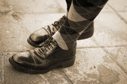 Black shiny broques with square pattern socks on a real person standing on pavement. Shot from above. Classic men's footwear in real environment photo