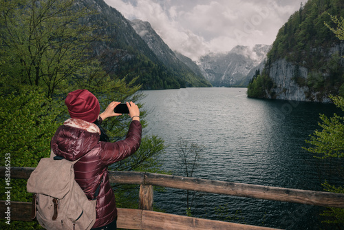 Germany. Berchtesgaden National Park. A girl with a mobile phone on a viewing platform with a view of the lake Konigssee