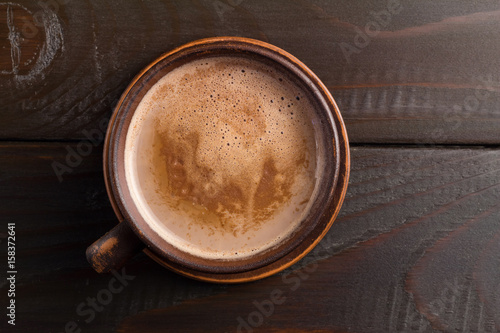 Hot chocolate or cocoa drink in clay cup, on dark brown wooden table, top view