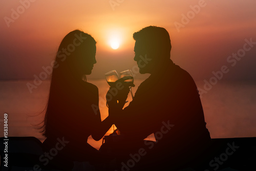 Silhouette of couple in love drinking wine during romantic dinner at sunset on the beach