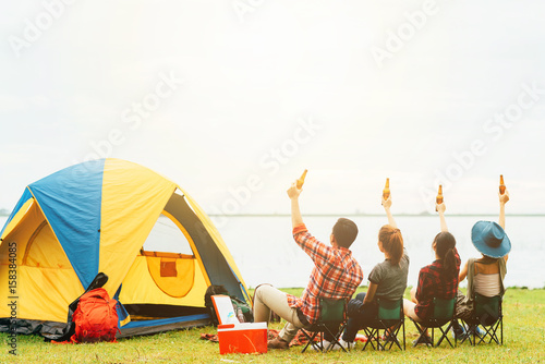 Back view of best friends raised arm with bottle of beer to celebrate while camping during travel.Friendship concept. photo