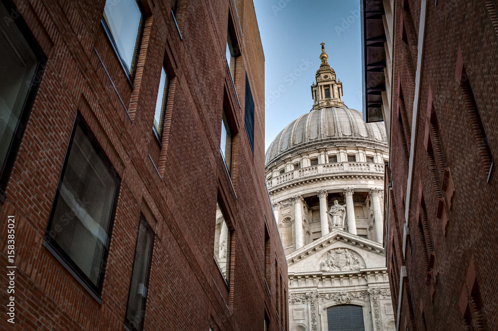 World renowned landmark that is St. Paul Cathedral seen from a narrow alley enclosed by two brick buildings on a sunny day of summer in London, England, UK
