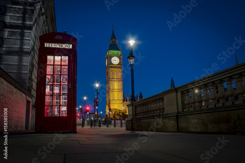 Traditional red phone booth or telephone box with the Big Ben in the background, possible the most famous English landmark, at night in London, England, UK photo