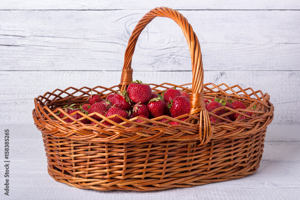 Wicker basket filled with ripe strawberries. On a white wooden background. Wicker basket filled with ripe strawberries. On a white wooden background.