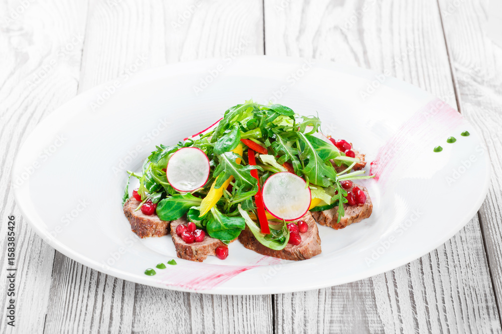 Salad with beef steak, baby spinach, lettuce, sweet pepper and grains of pomegranate on wooden background close up. Top view Salad with beef steak, baby spinach, lettuce, sweet pepper and grains of pomegranate on wooden background close up. Top view