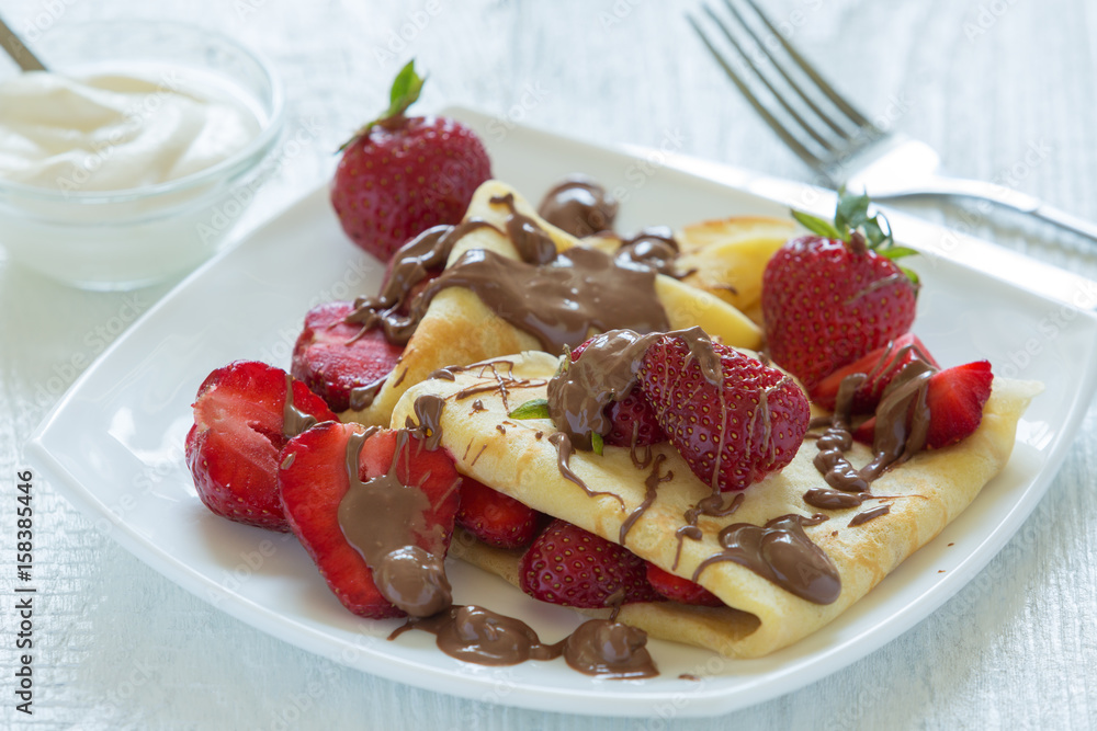 Pancakes with strawberries drizzled with chocolate. On a white wooden background. Pancakes with strawberries drizzled with chocolate. On a white wooden background.