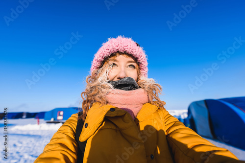 Close-up of a girl in a yellow down jacket pink knitted cap with red hair beautiful young hair in a hoarfrost in the background of the camp Barneo on a snowy north pole in winter