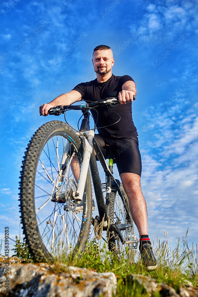 Bottom view of the smiling cyclist with bike against blue sky with clouds.