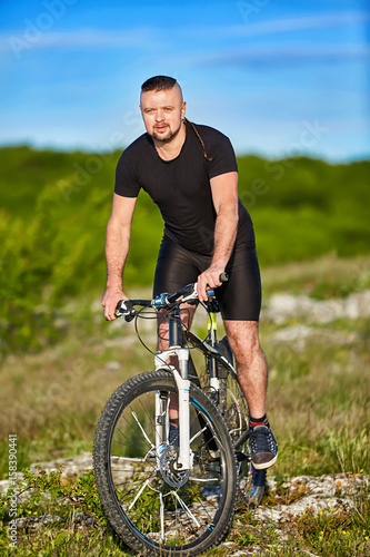 Portrait of athlete man riding mountain bike on the hill in summer season.